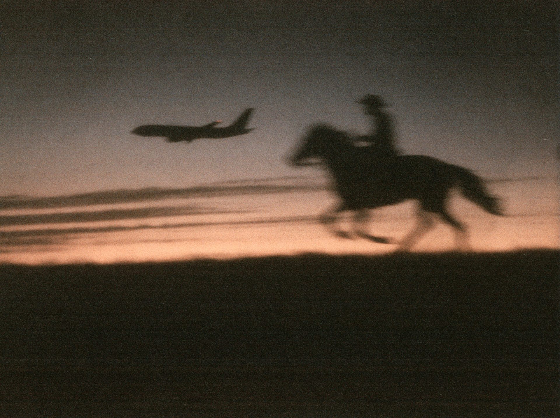 A rider on horseback at dusk as a jet climbs into the sunset behind them